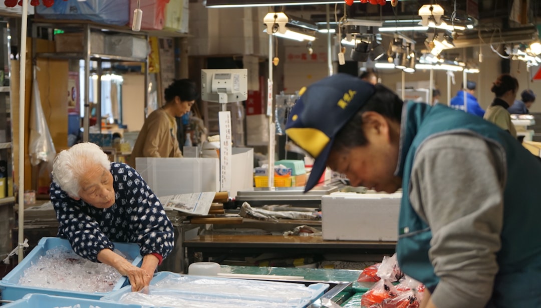 ChatGPT活用術：プロンプトからマルチモーダルまで、AIの真価を引き出す秘訣 - Elderly white haired Japanese woman in traditional apron working in the fishmarket with a middle aged man in baseball cap.