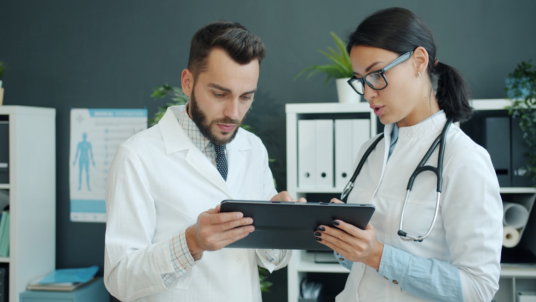 【ChatGPT】最新アップデート！ヘルスケア機能の強化を徹底解説 - Medics in white gowns young man and woman are using tablet at work talking using gadget in office. Modern devices, people and technology concept.