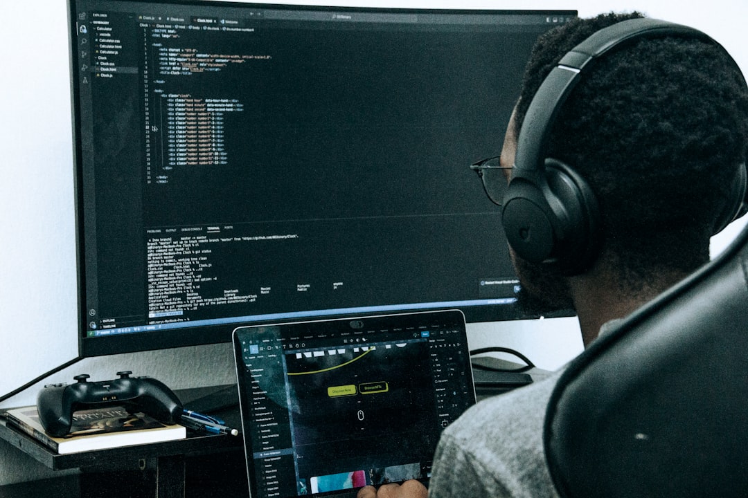 【Kiro】最新アップデートで「Tangent」機能が登場！作業効率を劇的に改善 - A focused developer working on code, using dual screens. The primary monitor displays a coding editor, while the laptop shows a UI design tool. Wearing headphones, the developer works in a quiet, minimal workspace, emphasizing productivity and tech innovation. Ideal for themes like coding, programming, web development, and tech workspace inspiration.